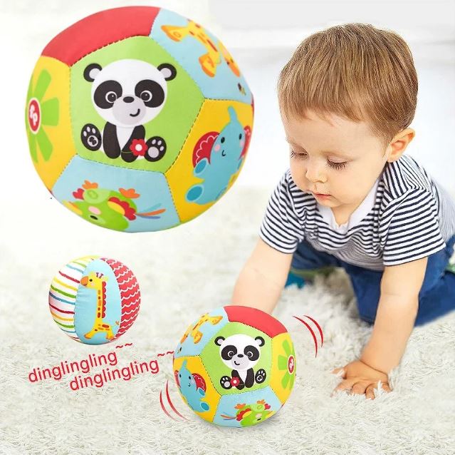 Enfant jouant avec une balle sensorielle en tissu présentant des motifs d'animaux colorés, émettant un son de clochette.