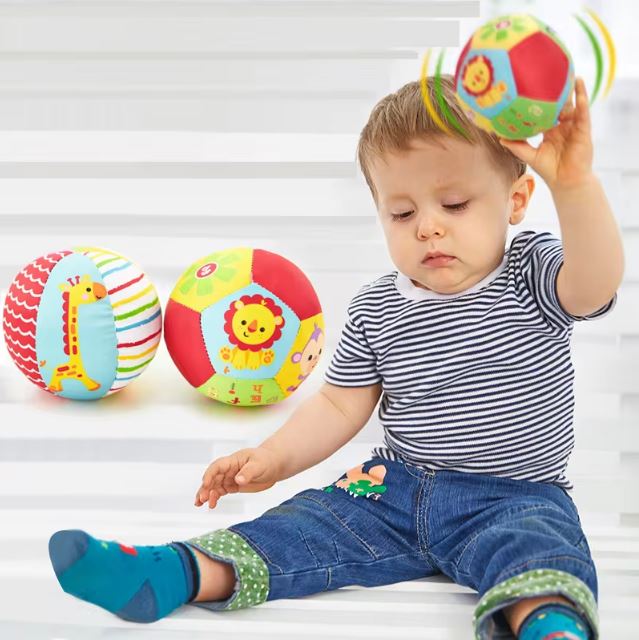 Un enfant jouant avec une balle sensorielle en tissu colorée, accompagnée de deux autres balles décorées d'animaux, idéales pour éveiller la curiosité des tout-petits.