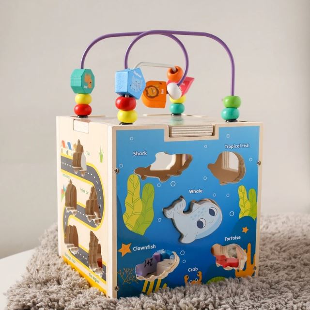 Cube en bois multi activités avec labyrinthe de perles et des formes d'animaux marins à encastrer, conçu pour encourager l'apprentissage et la motricité fine chez les enfants.