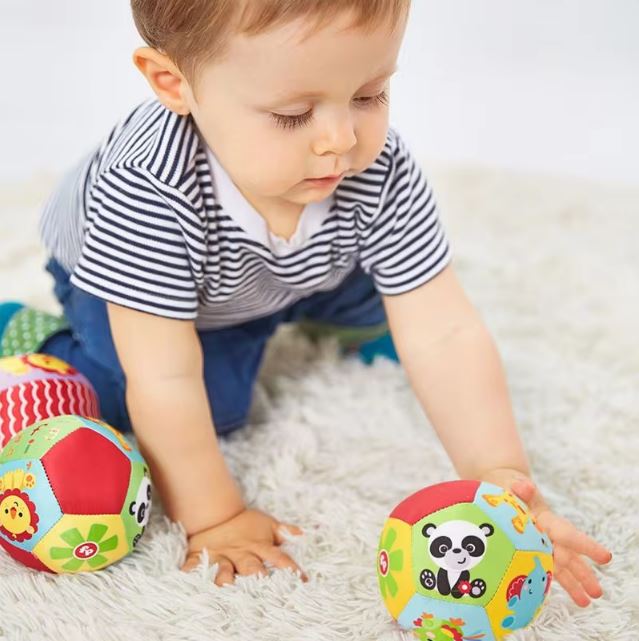 Bébé jouant avec une balle sensorielle en tissu, ornée de motifs d'animaux colorés, conçue pour stimuler les sens et encourager la motricité.