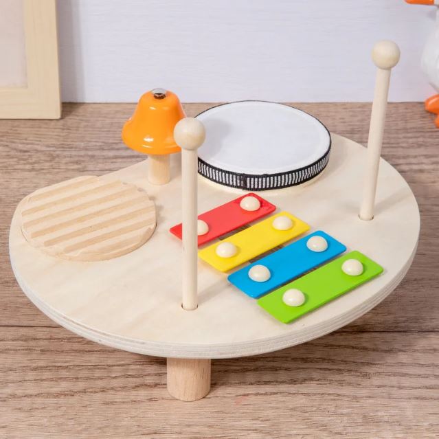 Table musicale Montessori en bois comprenant un xylophone coloré, un tambour, une cloche et un bloc sonore en bois, idéale pour l'éveil musical des petits.