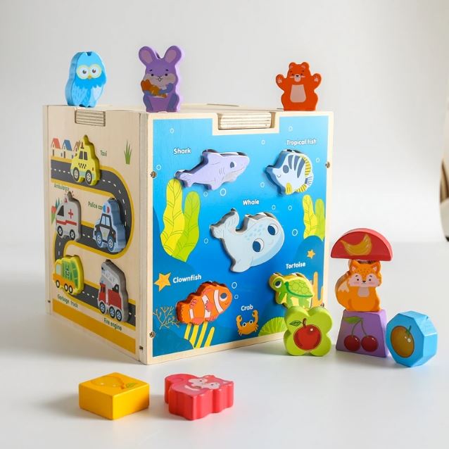 Cube en bois multi activités avec des formes d'animaux marins à encastrer, ainsi que des formes colorées d'animaux et de fruits pour stimuler la créativité et la motricité des enfants.