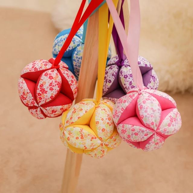 Ensemble de balles sensorielles Montessori colorées en tissu floral, suspendues avec des rubans, idéales pour le développement tactile et sensoriel des enfants.