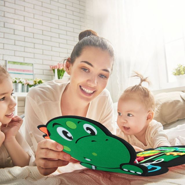 Maman et ses enfants partageant un moment de jeu avec un livre d'activités sensorielles en tissu en forme de dinosaure.