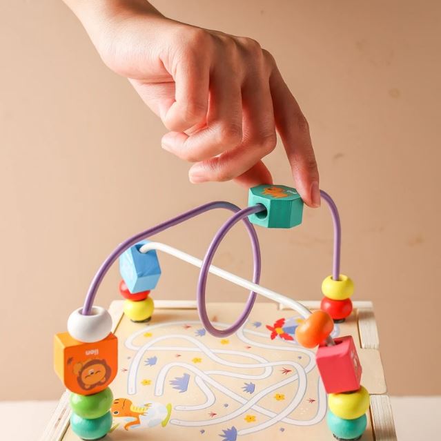 Main déplaçant des perles d'un labyrinthe de perles d'un cube en bois multi activités, stimulant la coordination et la dextérité des enfants en bas-âge.