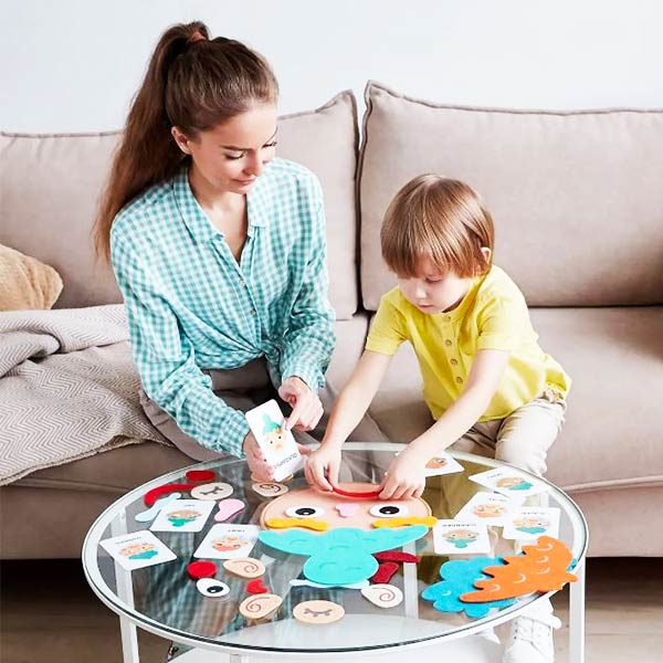 Un Enfant et un adulte jouant ensemble avec un visage des émotions Montessori, disposé sur une table. L’enfant place des éléments de visage, pour exprimer différentes émotions.