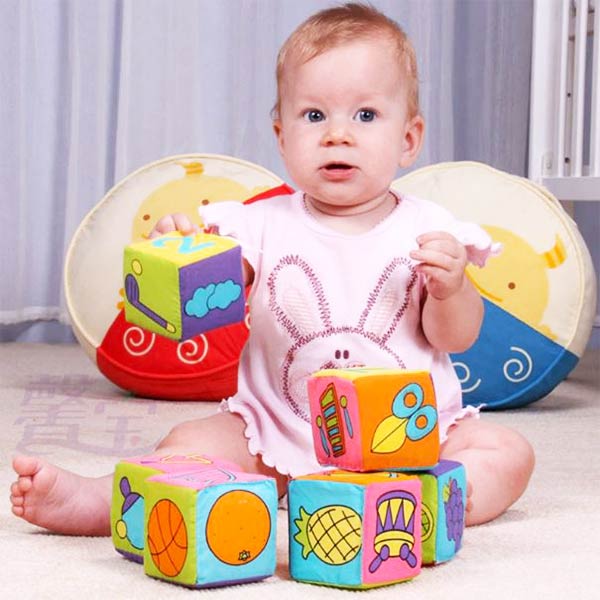 Bébé jouant avec des cubes montessori en tissu aux motifs colorés et éducatifs, parfaits pour développer la motricité et l'éveil sensoriel dès le plus jeune âge.