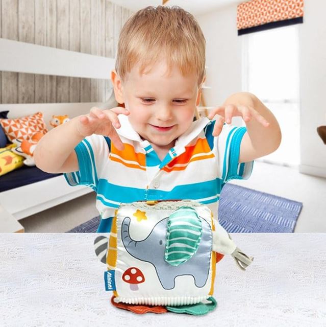 Enfant jouant avec un cube d'activité en tissu pour bébé décoré d'un éléphant et de textures variées, stimulant l'éveil sensoriel et la motricité.