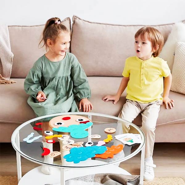 Deux enfants assis sur un canapé, interagissant joyeusement autour d'un jeu visage des émotions Montessori disposé sur une table en verre.