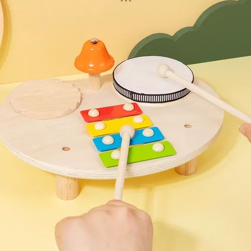 Enfant jouant avec une table musicale Montessori en bois, incluant un xylophone, un tambour, une cloche et un bloc sonore en bois.