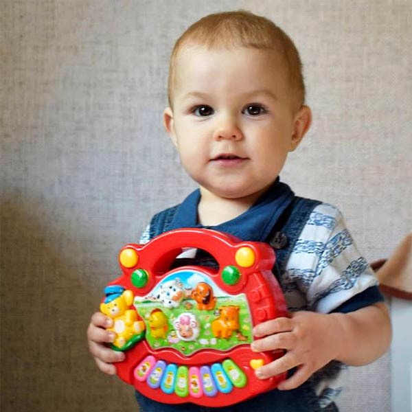 Bébé tenant un piano éducatif coloré, conçu pour stimuler l'éveil musical et sensoriel à travers des touches lumineuses et des sons d'animaux.