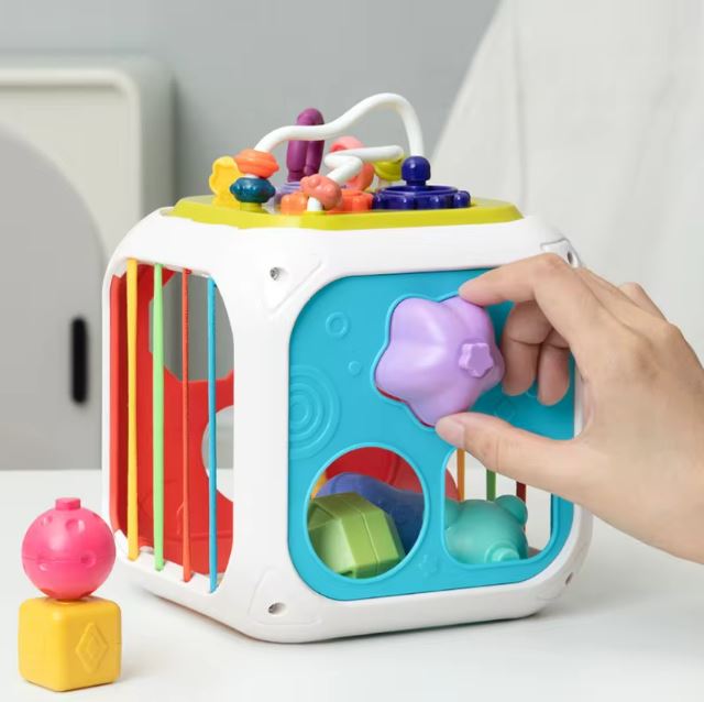 Cube d'éveil sensoriel avec formes à insérer et éléments interactifs, favorisant le développement de la coordination et les capacités sensorielles des bébés.