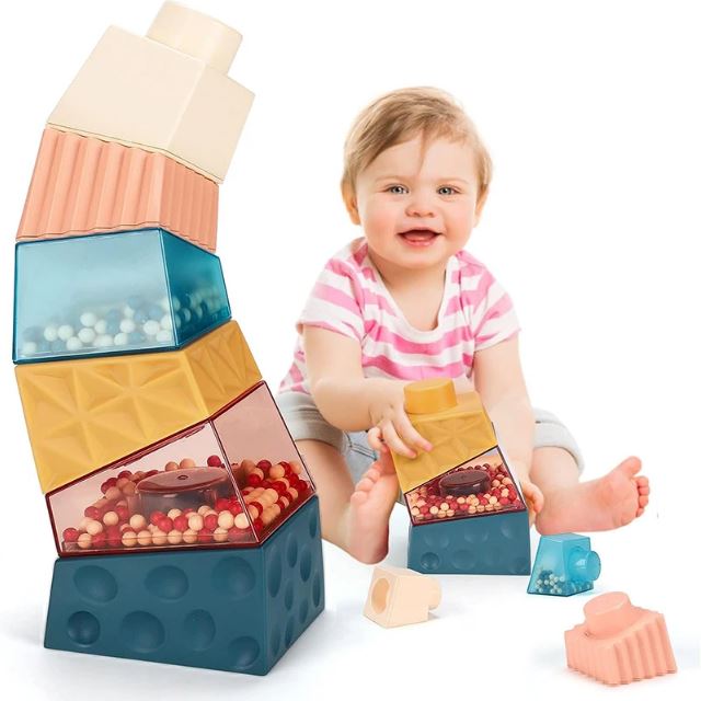 Bébé souriant jouant avec des cubes à empiler montessori colorés, conçus pour développer la coordination, la motricité et la créativité à travers l'empilement et l'exploration sensorielle.