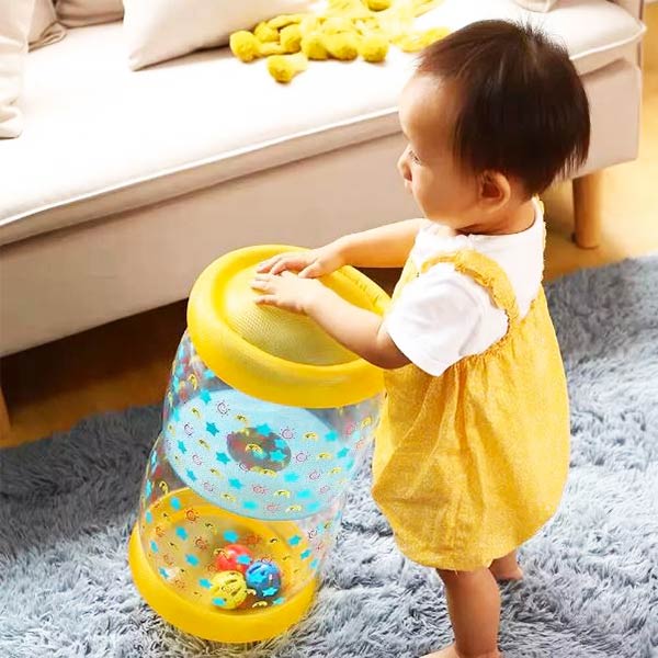 Un bébé debout qui s'amuse avec un rouleau gonflable transparent, parfait pour l'aider à développer son équilibre et à explorer en toute sécurité.